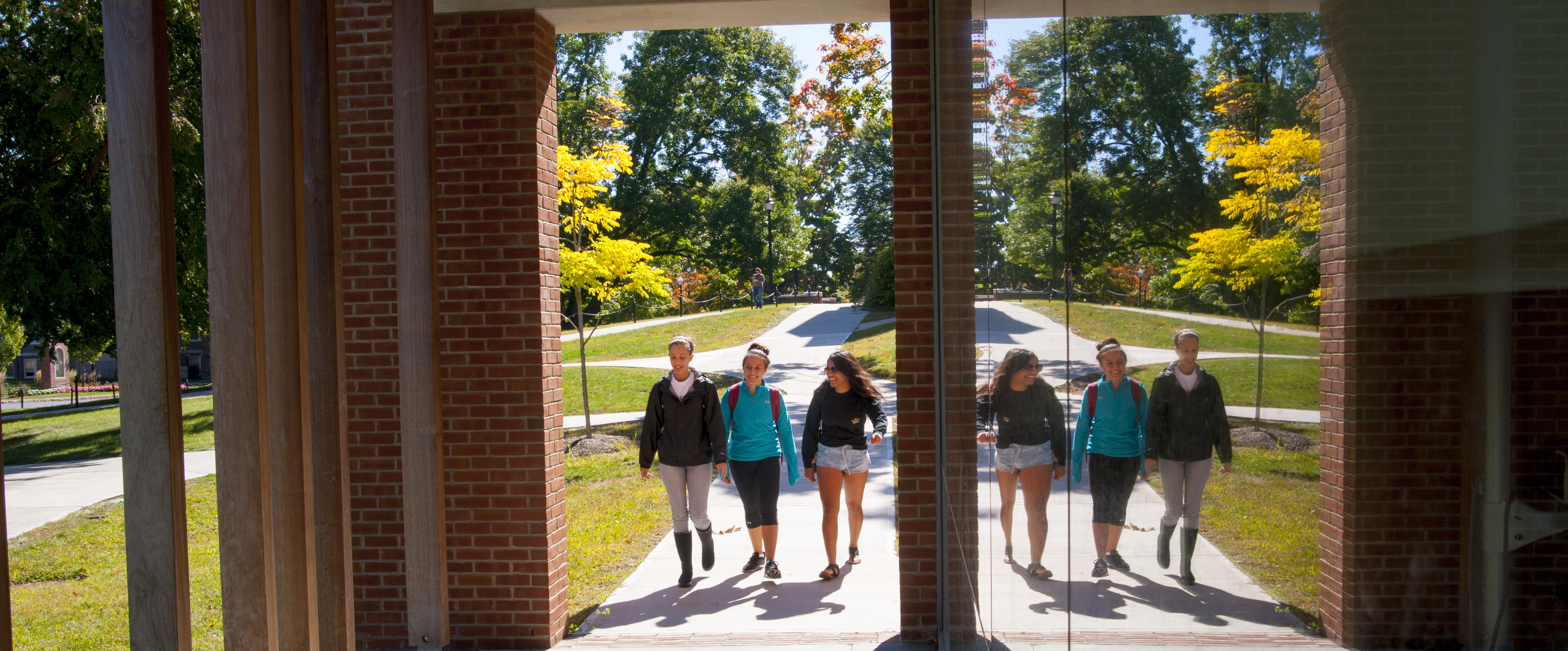 Three students walk under the front portico of Storrs Hal