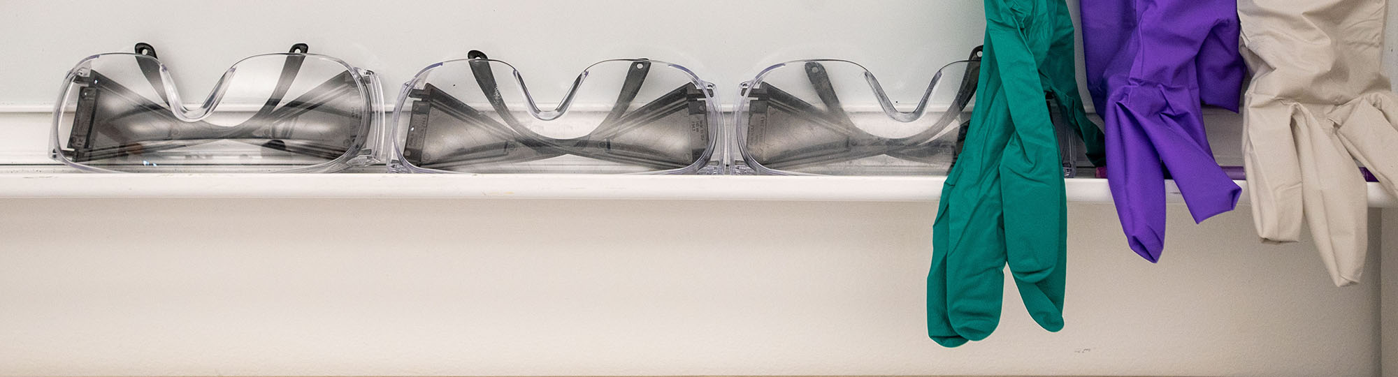 Goggles and gloves lined up against a whiteboard.