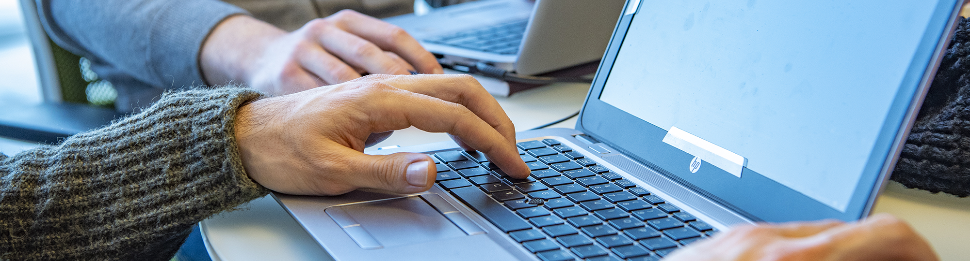 Two people type on laptops